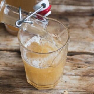 a bottle of yellow ginger beer being poured into a glass on a wooden board