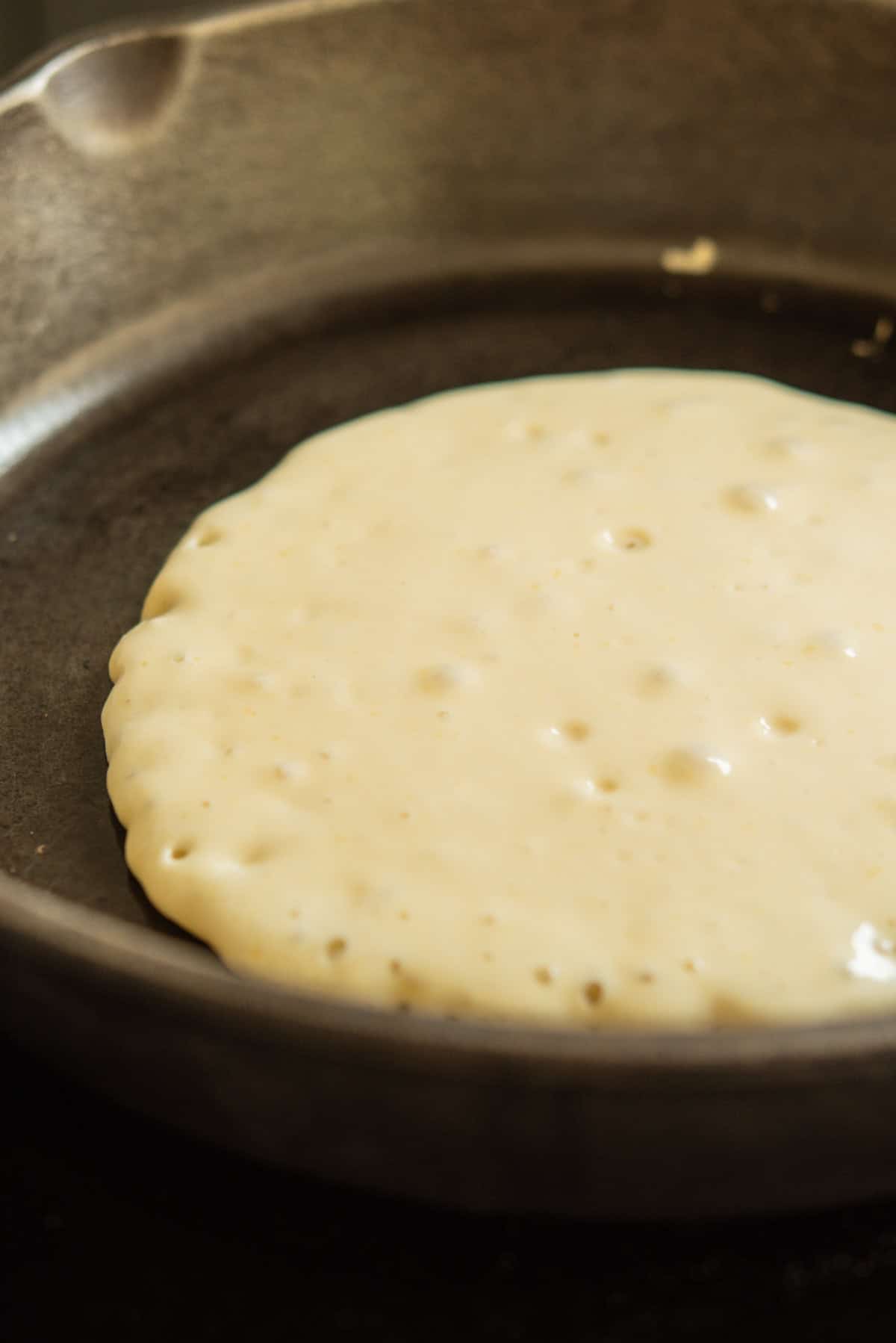 A sourdough discard pancake cooks in a skillet, with bubbles forming on the surface as it rises and cooks to perfection.