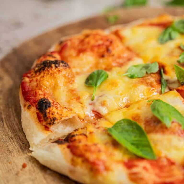 Close-up of a cheese pizza with melted cheese, tomato sauce, and fresh basil leaves on a wooden surface. One slice, made with a delicious sourdough pizza crust recipe, is slightly pulled out from the whole pizza.