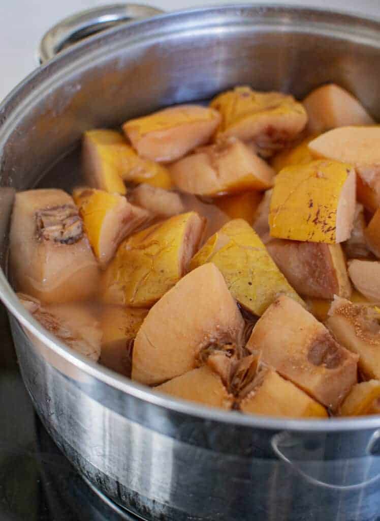 Cooked quince pieces in water in a silver pot