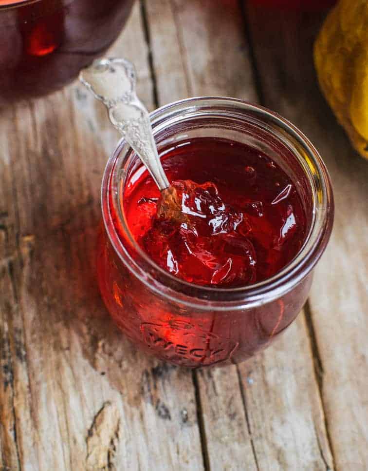 A jar of red quince jelly on a wooden board with a spoon in it 