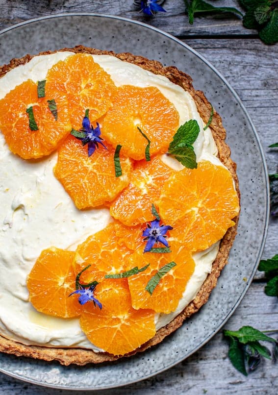 top down view of a lemon yogurt tart with slices of orange and mint on top, sitting on a grey plate