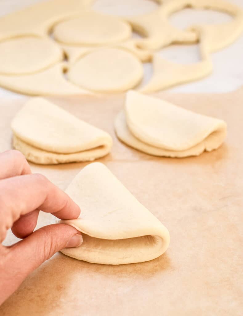 a hand that is folding bao dough pieces in half  