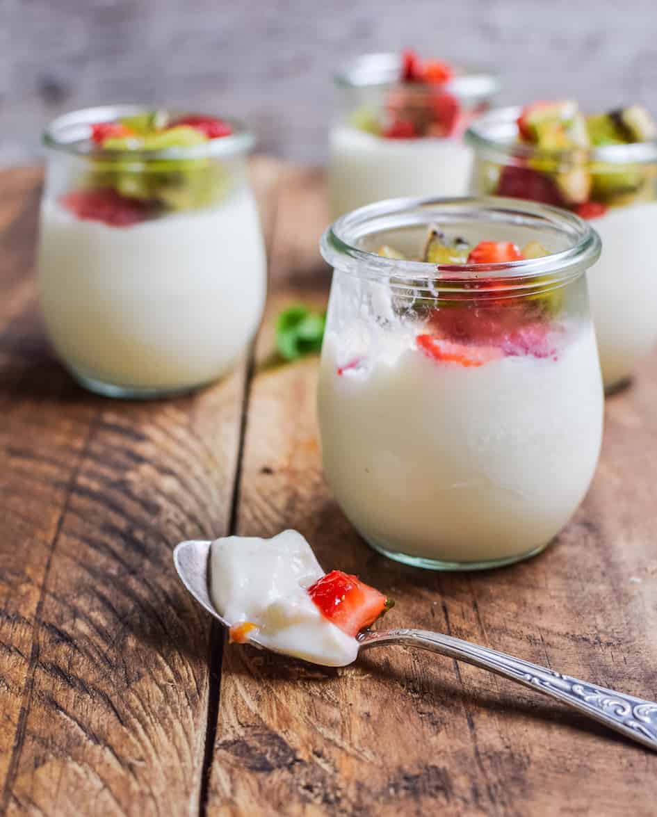 side view of yogurt panna cotta jars on a wooden table and  spoon full of panna cotta sitting on top