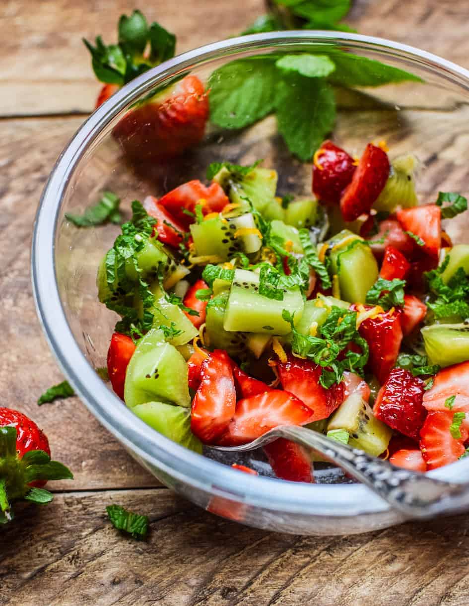 a bowl of chopped strawberries and kiwifruit in a glass bowl on a wodden table