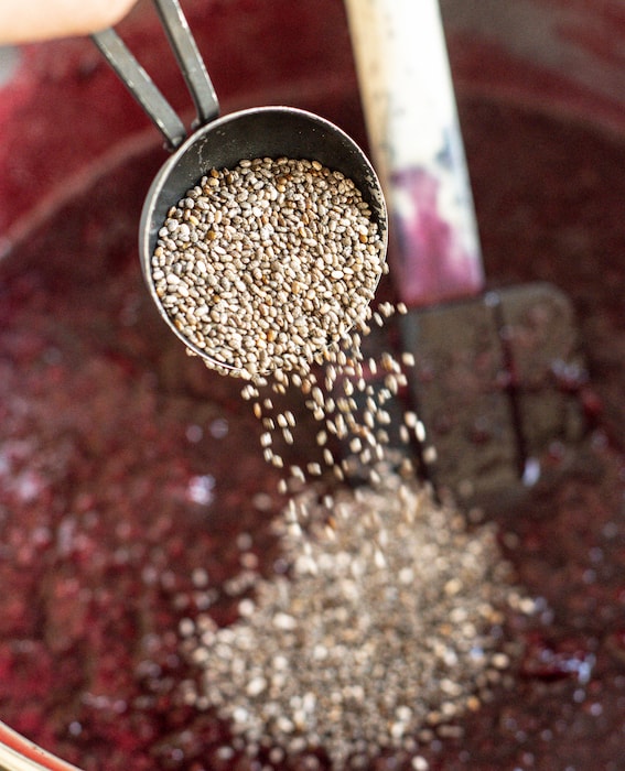 a spoon of chia seeds being poured into blackberry jam 
