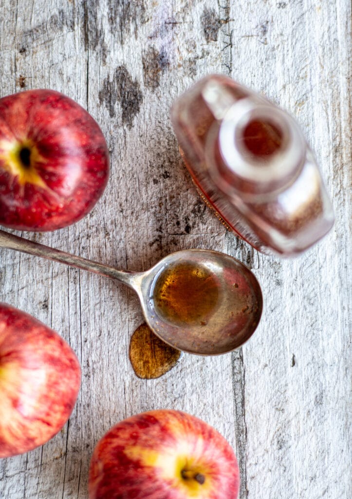 a birds eye view of apple syrup on a wooden bench with 3 red apples
