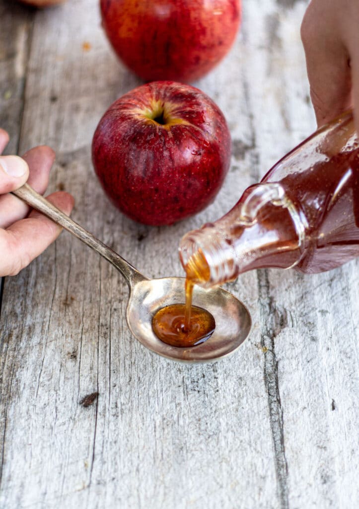 apple syrup being poured into a spoon with a red apple sitting on a wooden table