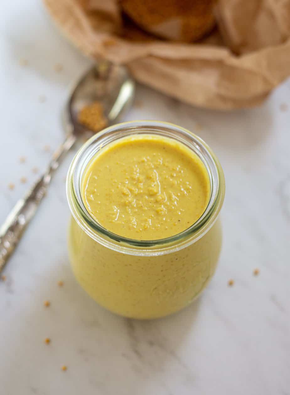 a jar of yellow mustard with a spoon in the background