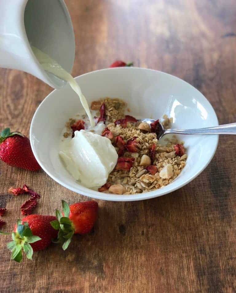 milk being poured over a bowl of strawberry muesli