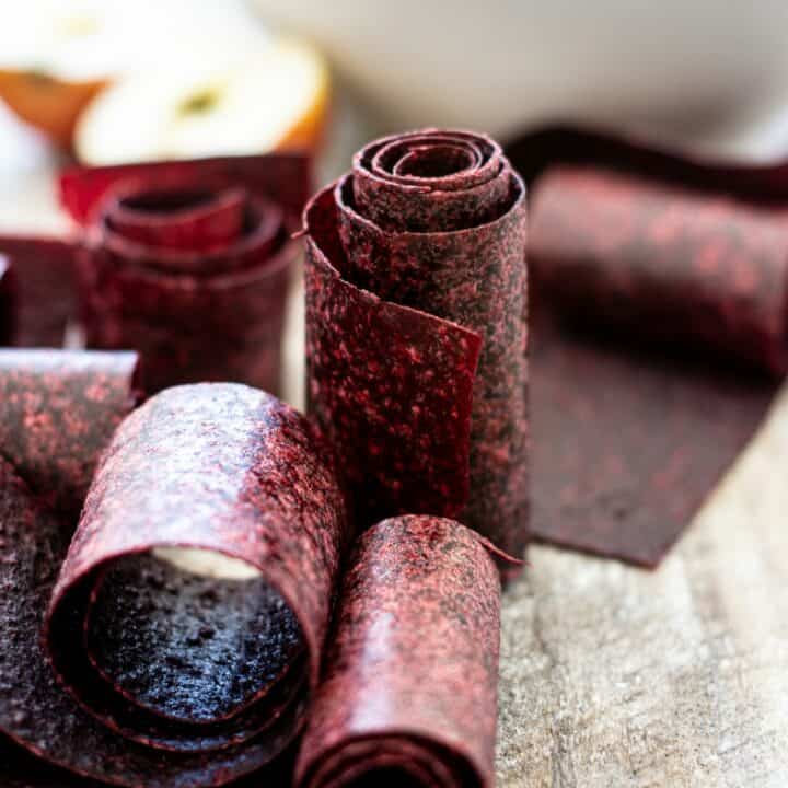 fruit leather rolls on a wooden board with a bowl of berries in the background