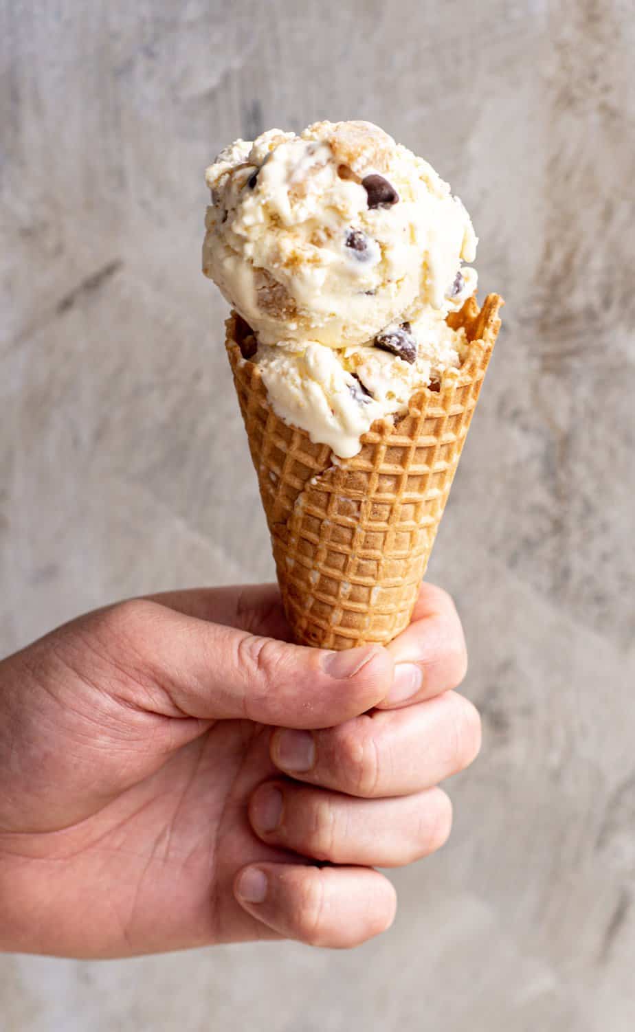 a hand holding an ice cream cone of cookie dough ice cream