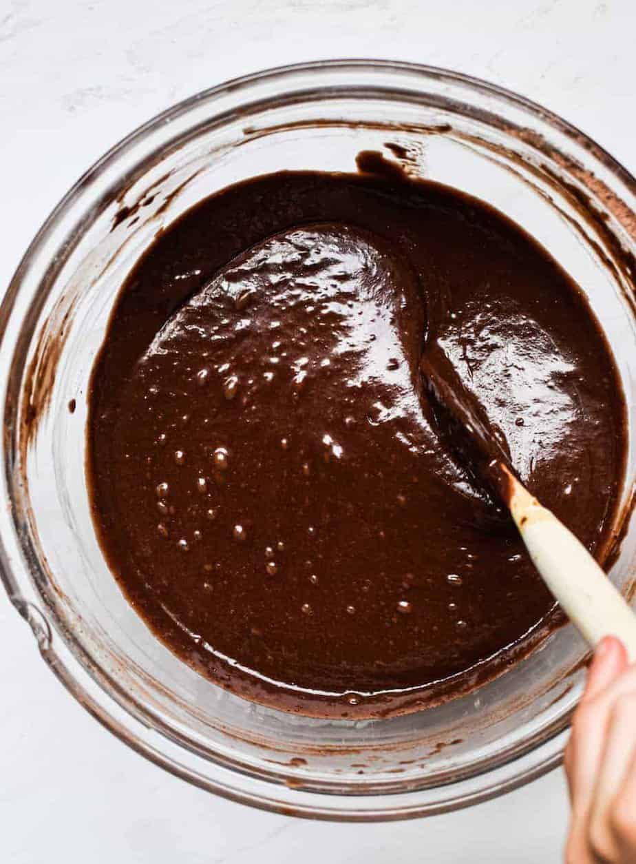 A glass bowl of chocolate Cake batter being stirred with a spatula