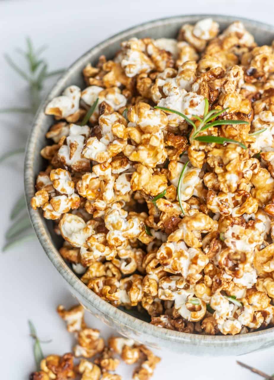 a side view close up of a bowl of caramel popcorn with green rosemary