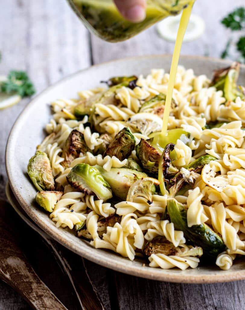 dressing being poured over a bowl of fusilli pasta with roasted Brussels sprouts and lemon