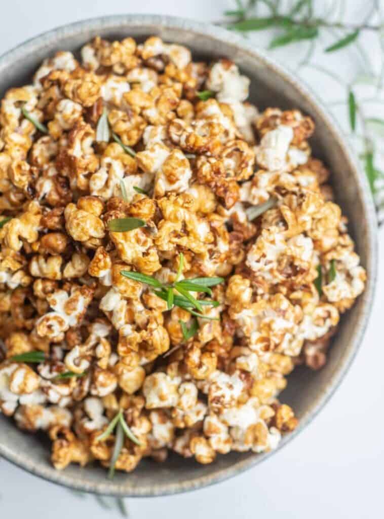 a bird's eye view close up of a bowl of caramel popcorn with green rosemary