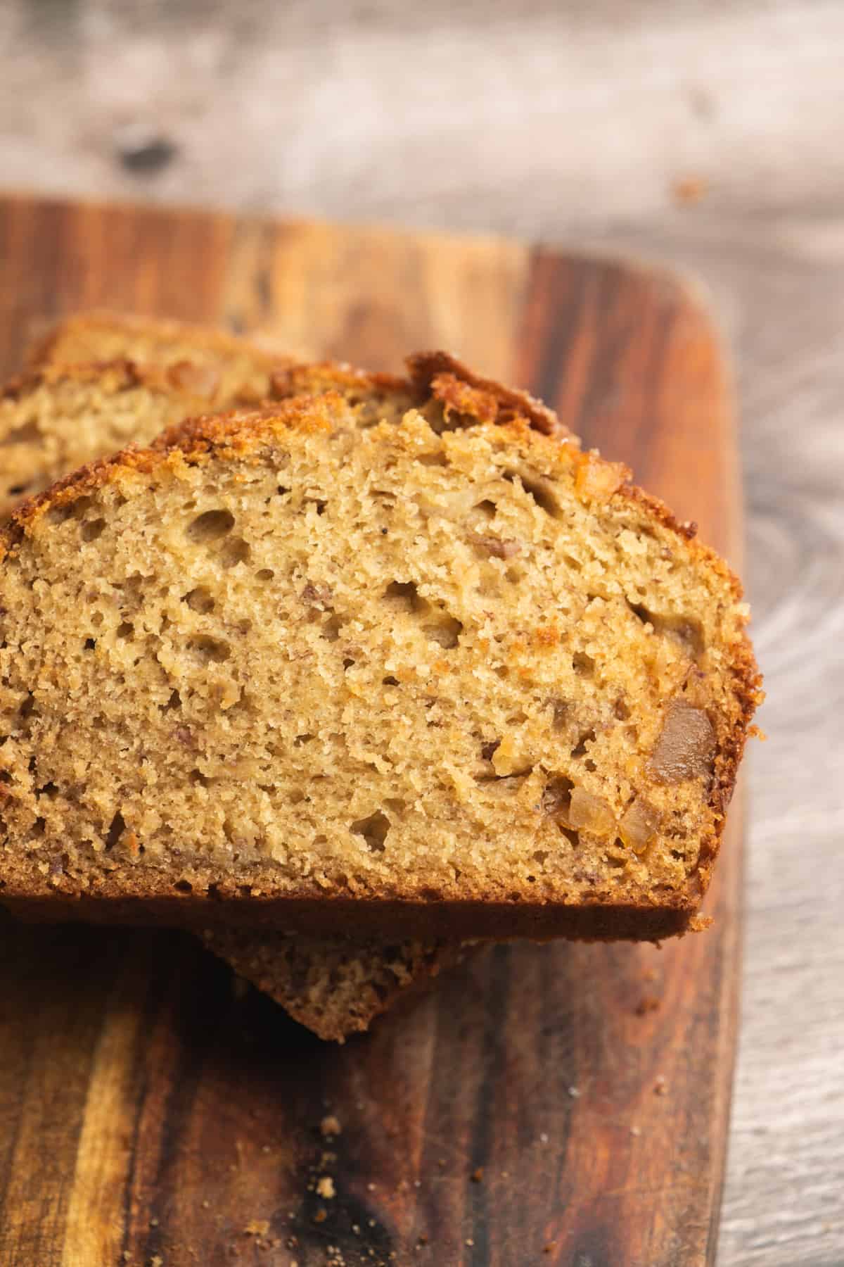 Two slices of moist Sourdough Banana Bread with a golden-brown crust rest on a wooden cutting board.