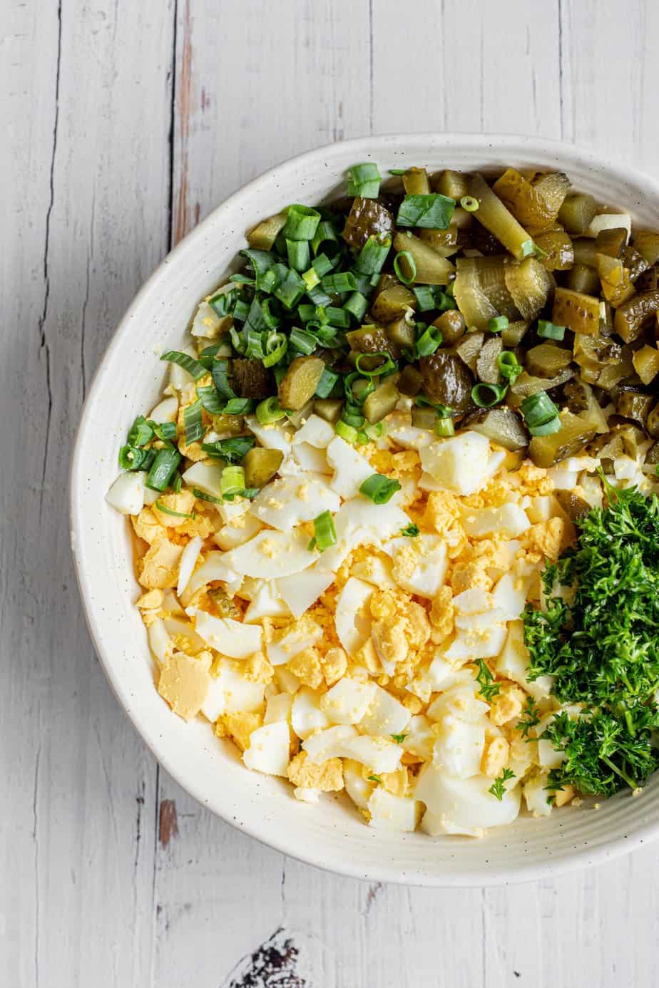 a bowl of egg salad with pickles and parsley