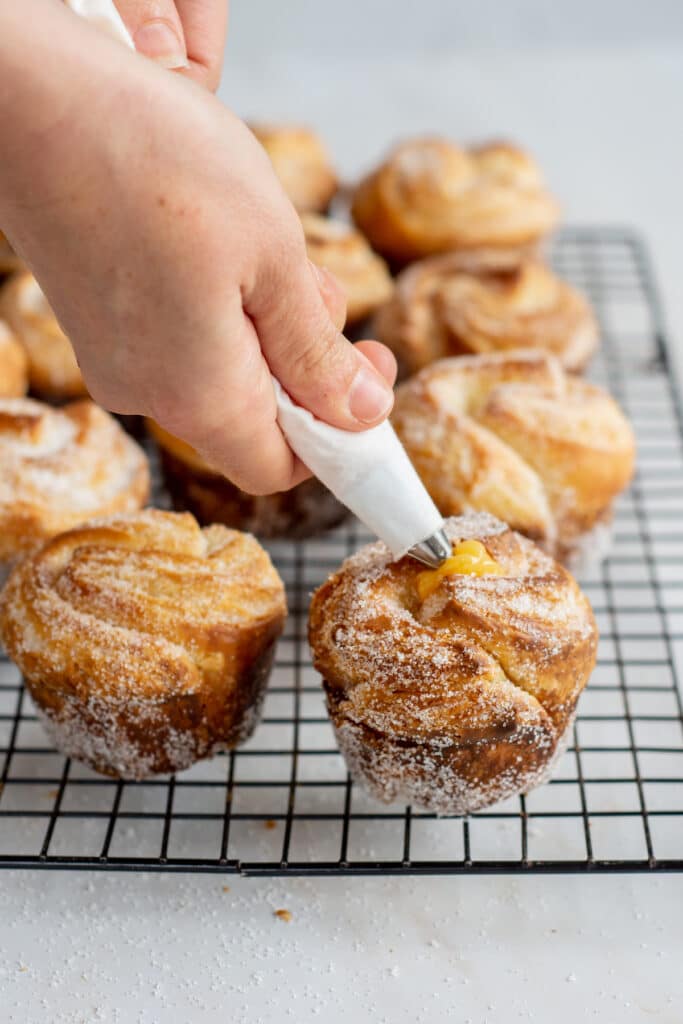 a hand piping lemon curd into cruffins