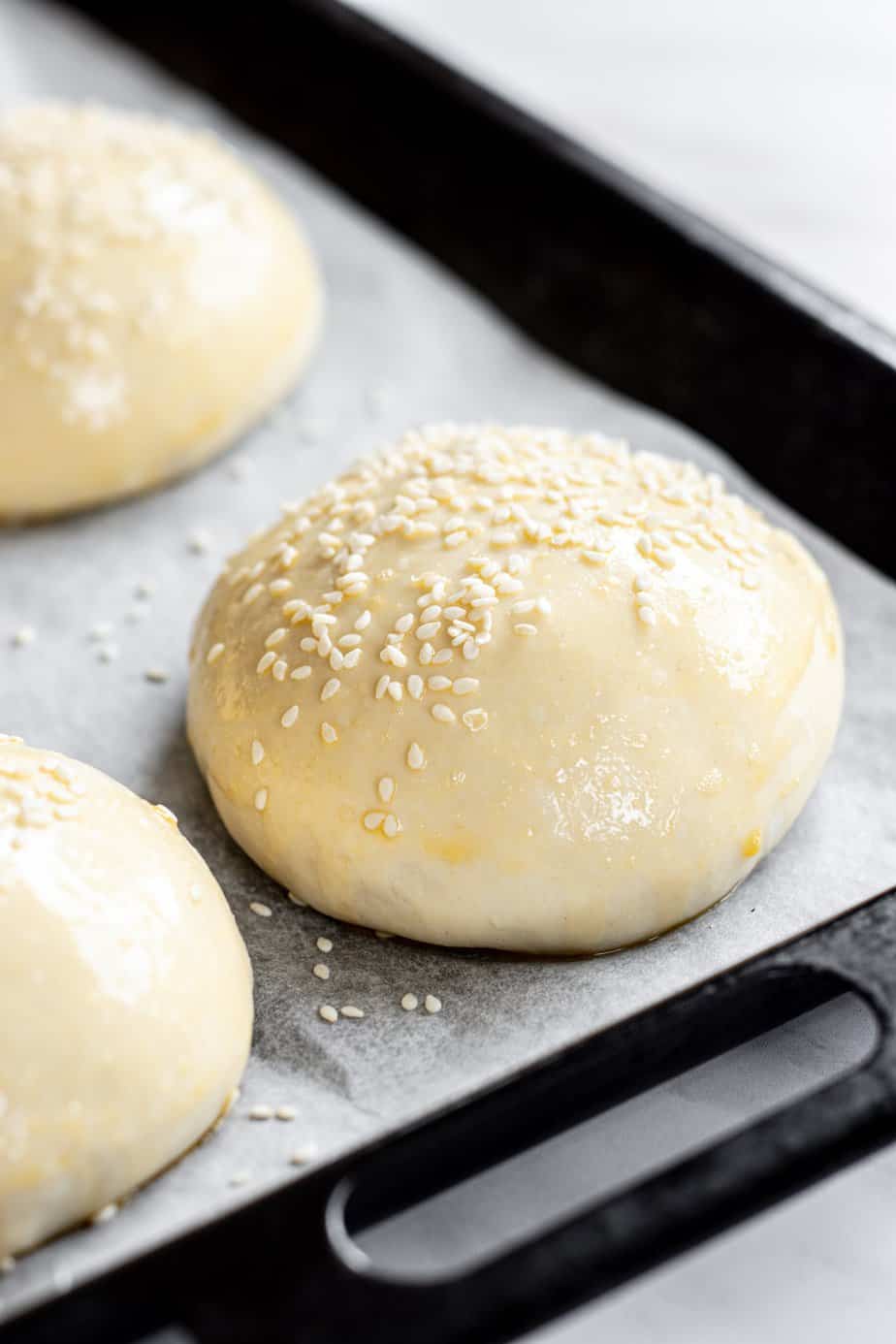 shaped burger bun rising with egg wash and sesame seeds