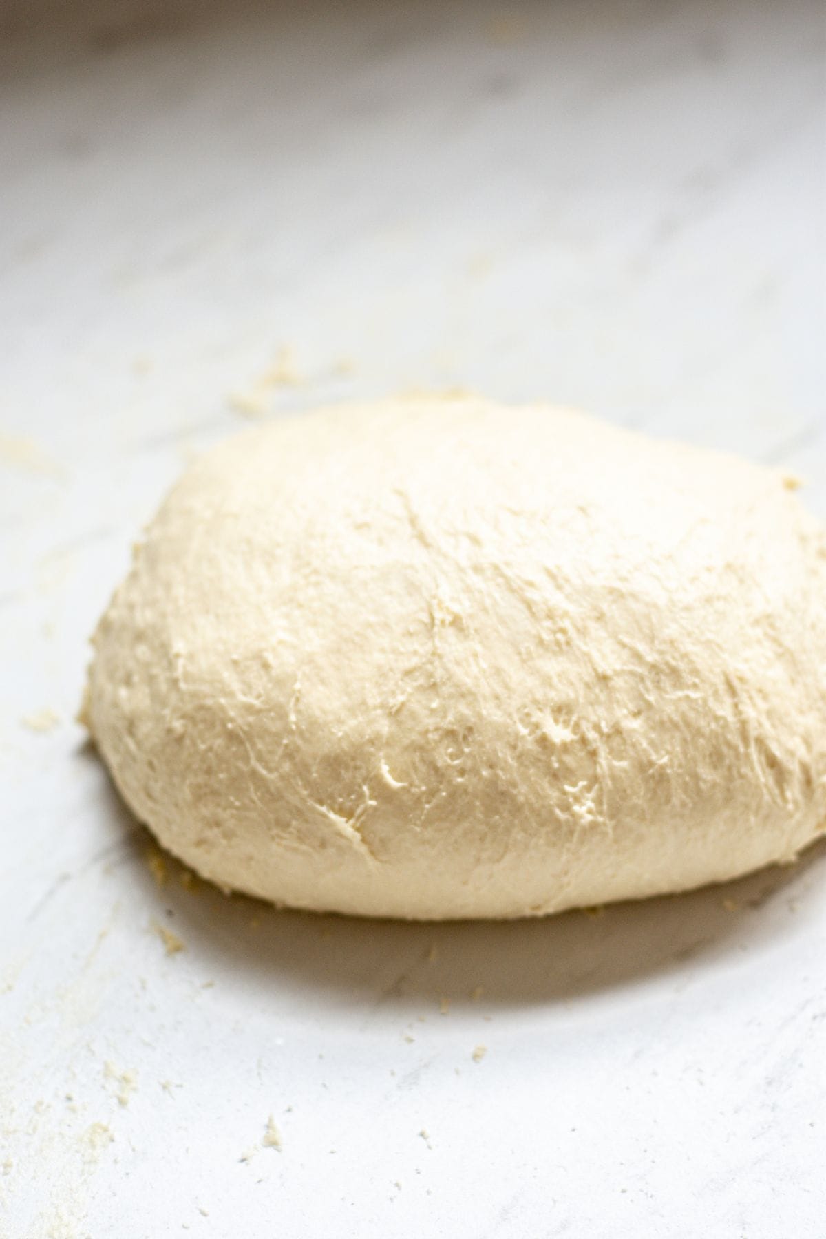 A ball of raw bread dough rests on a lightly floured white surface, ready to be shaped into delicious sourdough garlic knots or baked as desired.