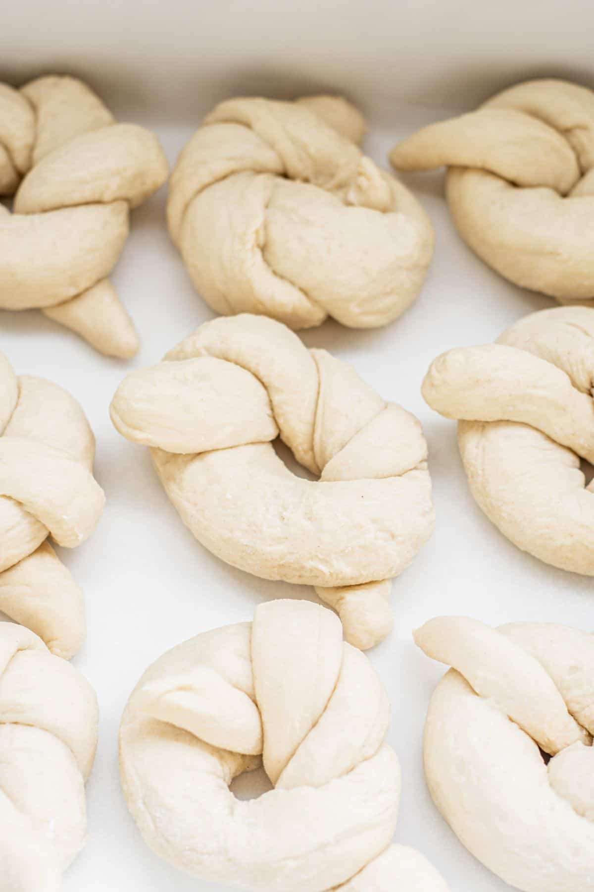 Unbaked sourdough garlic knots are twisted into rings and arranged closely together on a white surface, ready for baking.