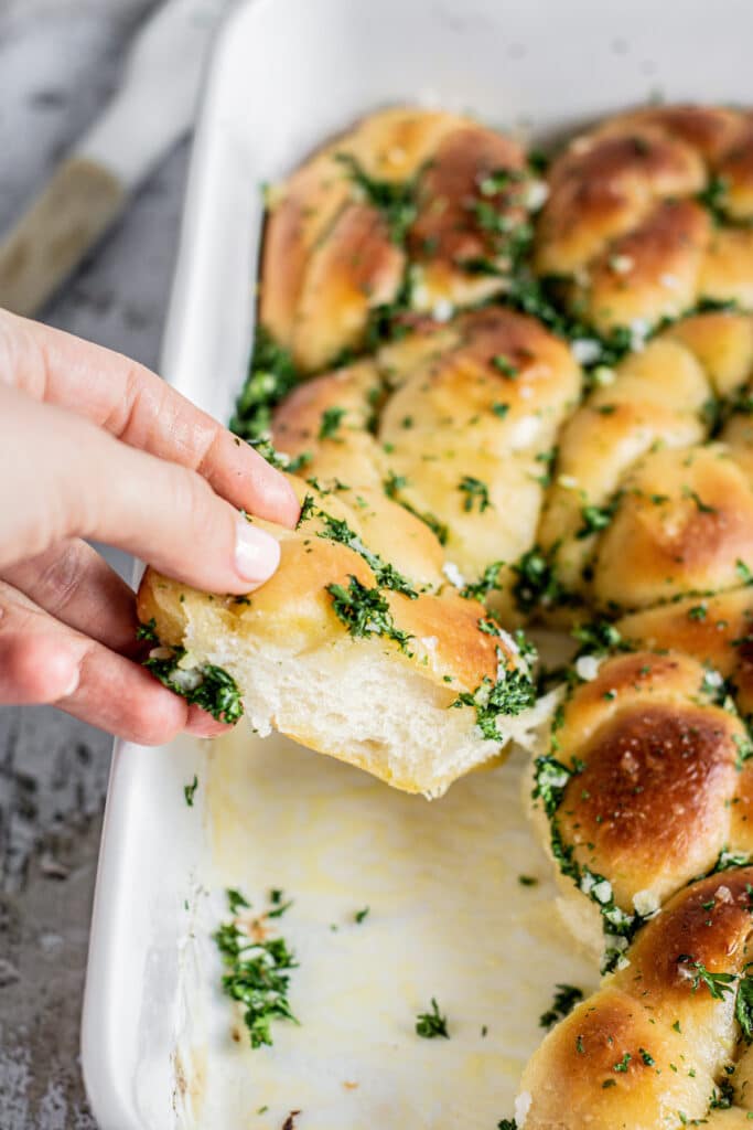 a hand pulling a garlic bread knot from a tray.