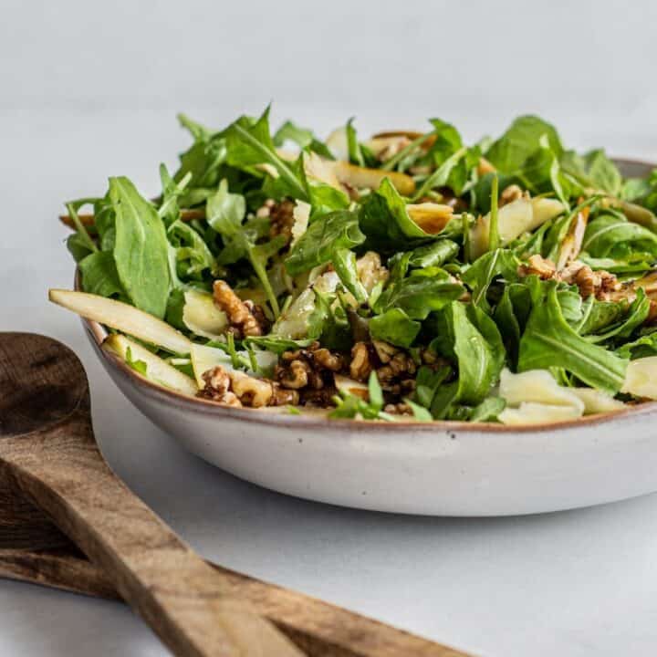 rocket pear and walnut salad in a bowl with salad tongs on the side.