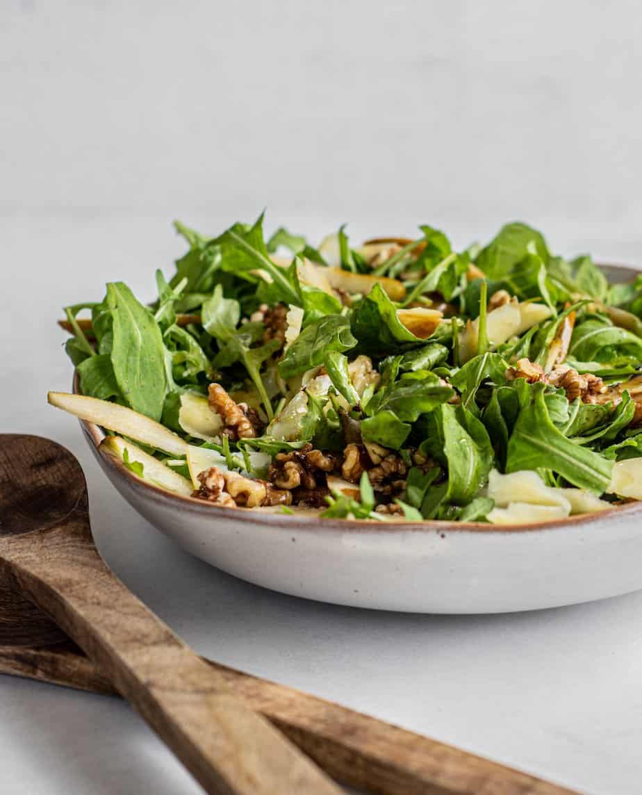 rocket pear and walnut salad in a bowl with salad tongs on the side.