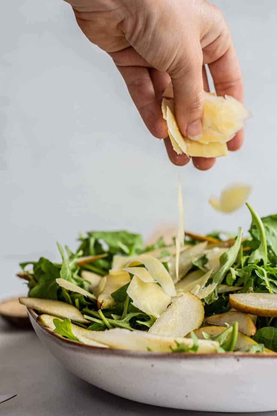 a hand adding shaved parmesan to salad.