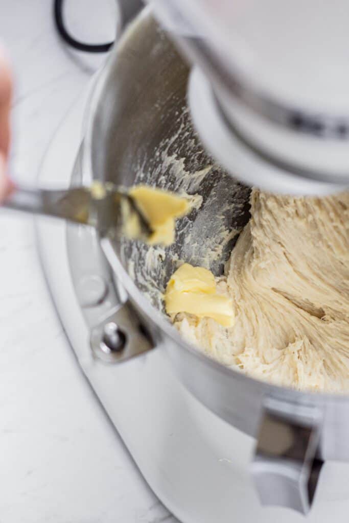 dough in a stand mixer with butter being added.