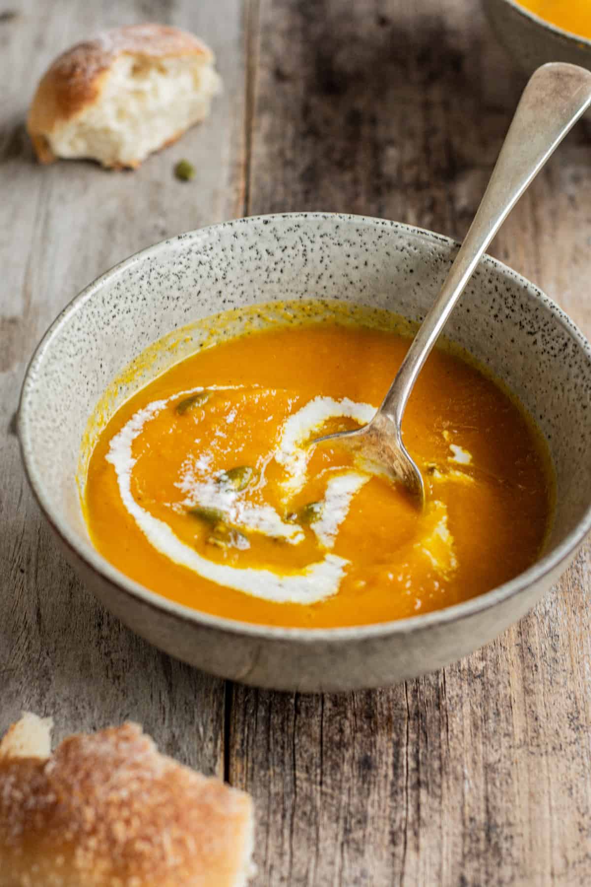 a spoon in orange soup swirled with yogurt.