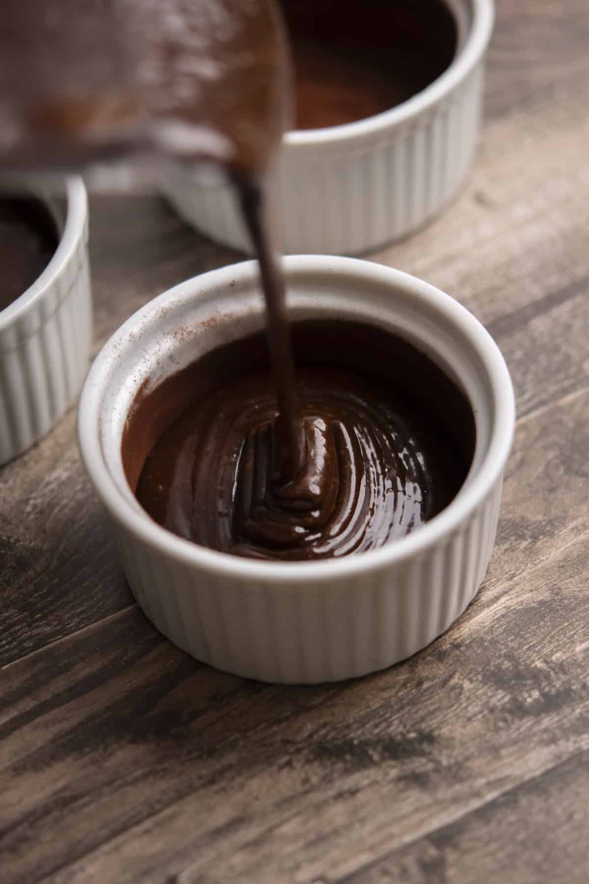 Rich chocolate batter is poured into a white ramekin.