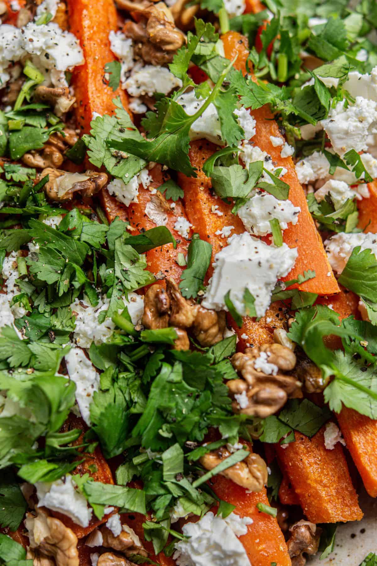 Close-up of roasted carrot sticks topped with crumbled feta cheese, chopped fresh cilantro, and walnut pieces.
