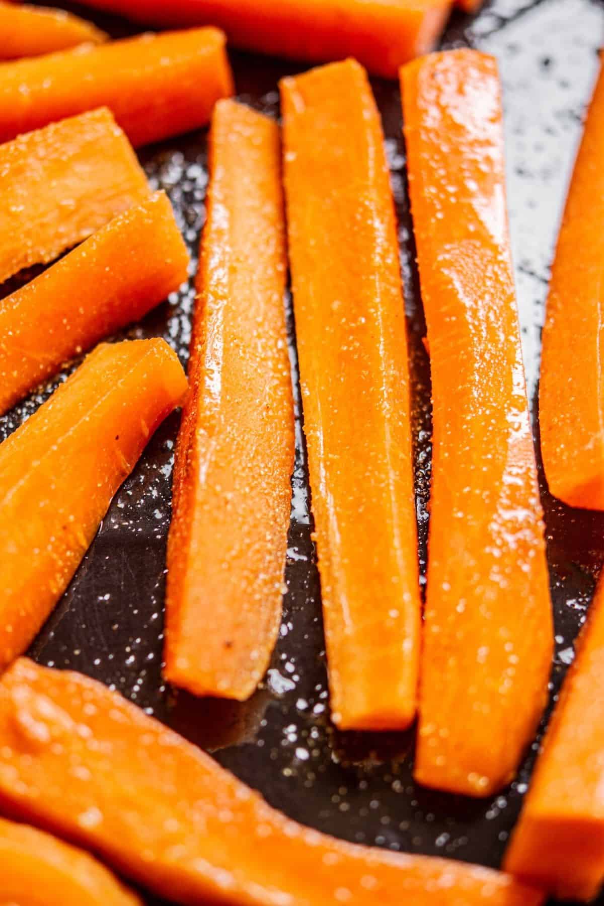 Close-up of sliced carrots arranged on a dark baking tray, lightly coated with oil and sprinkled with salt, ready for roasting.