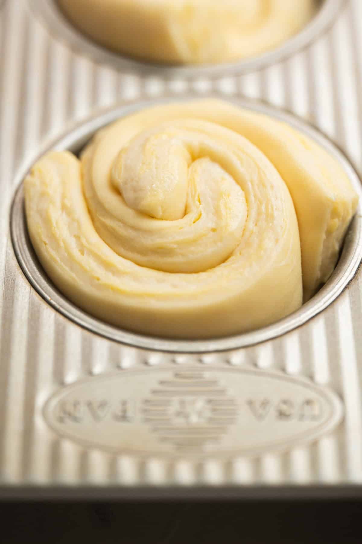A close-up of unbaked, swirled dough in a round slot of a metallic baking pan, ready to be baked.
