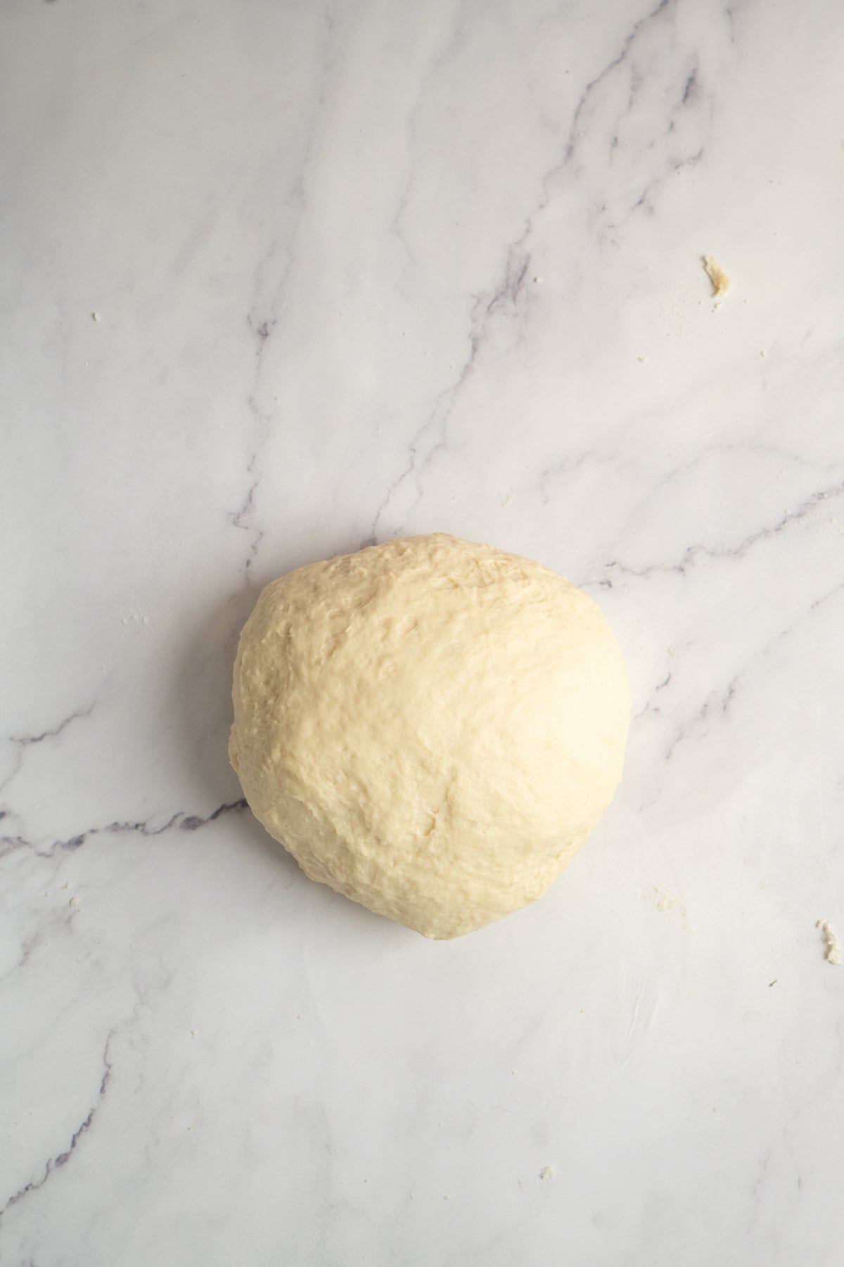 A ball of raw dough sits on a white marble surface, ready to be shaped or baked.
