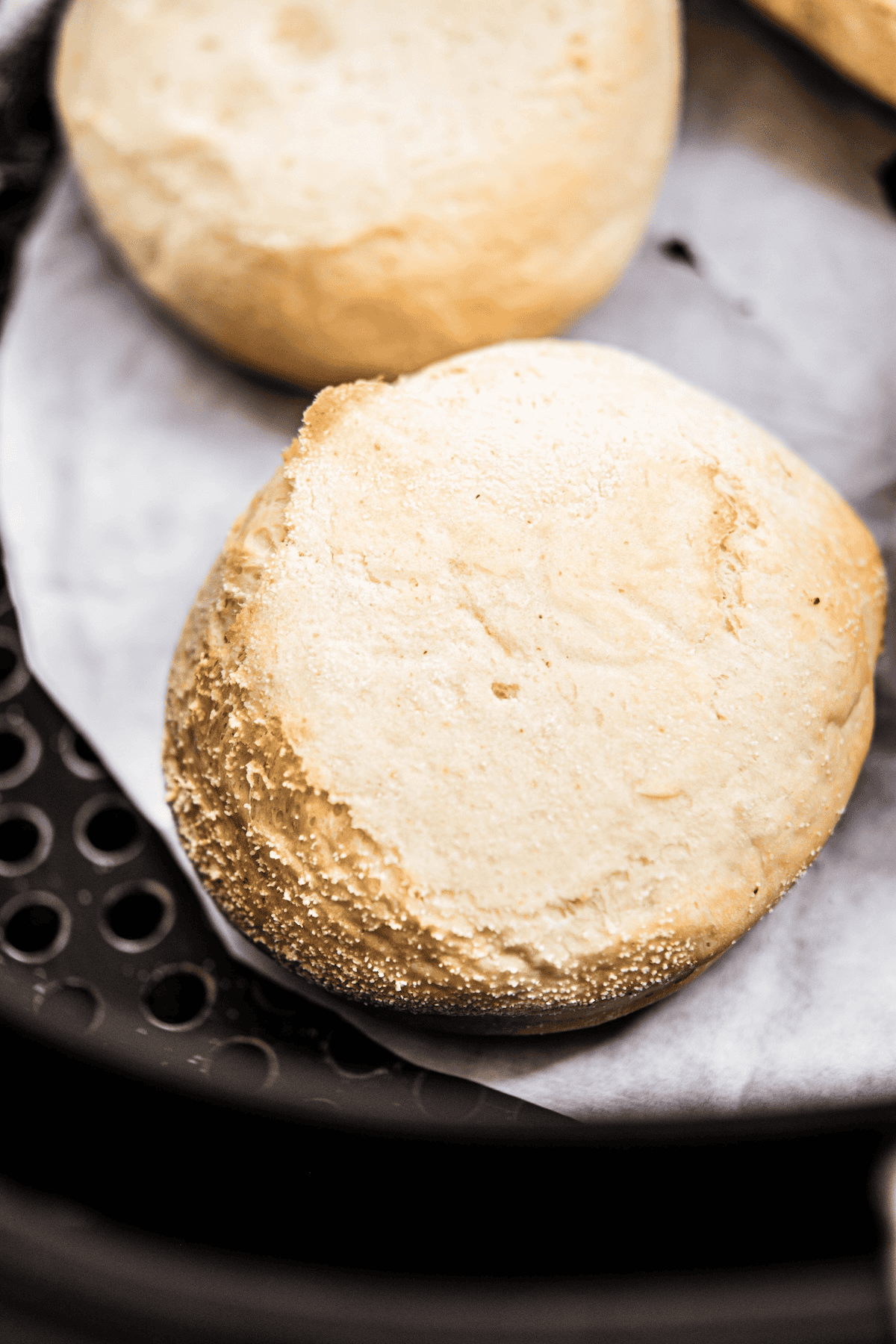 A close-up of a golden brown English muffin resting on parchment paper inside an air fryer basket.