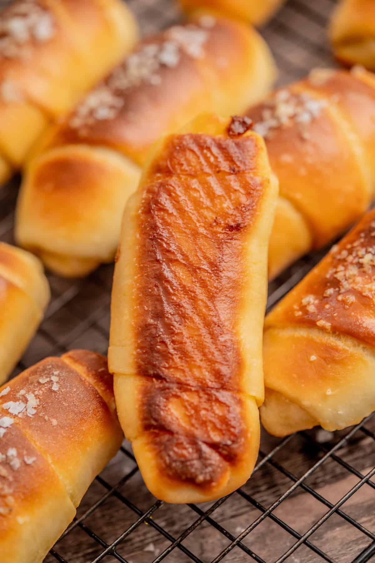 sourdough salt bread, one with a distinct grilled pattern on top, arranged on a wire cooling rack. Some rolls are sprinkled with coarse salt.