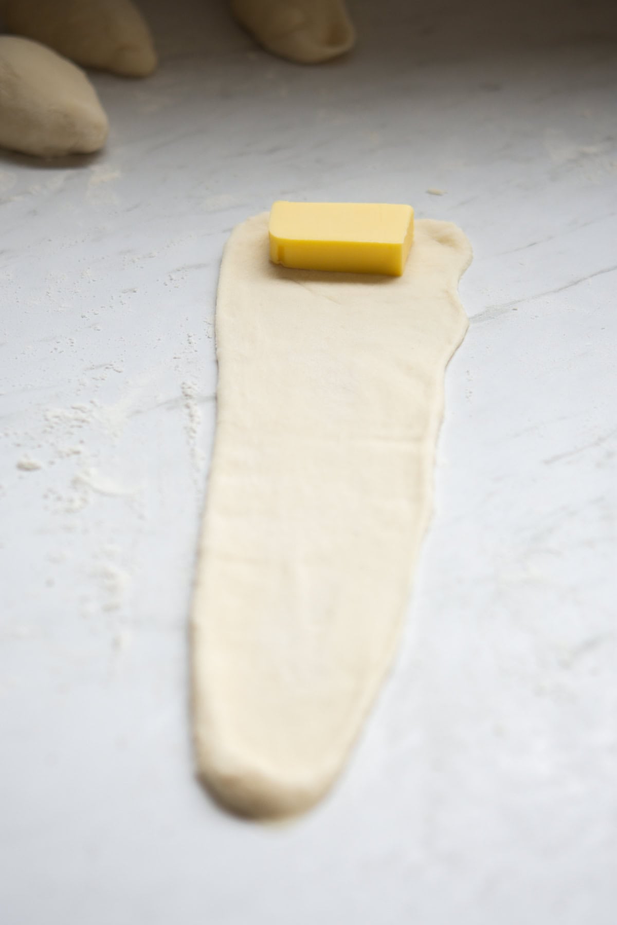 A rectangular piece of butter sits on one end of a long, thin strip of rolled-out dough on a lightly floured, white surface.