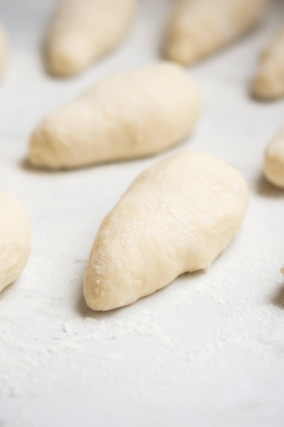 Several pieces of raw dough shaped into small, elongated ovals rest on a lightly floured surface, ready for baking.
