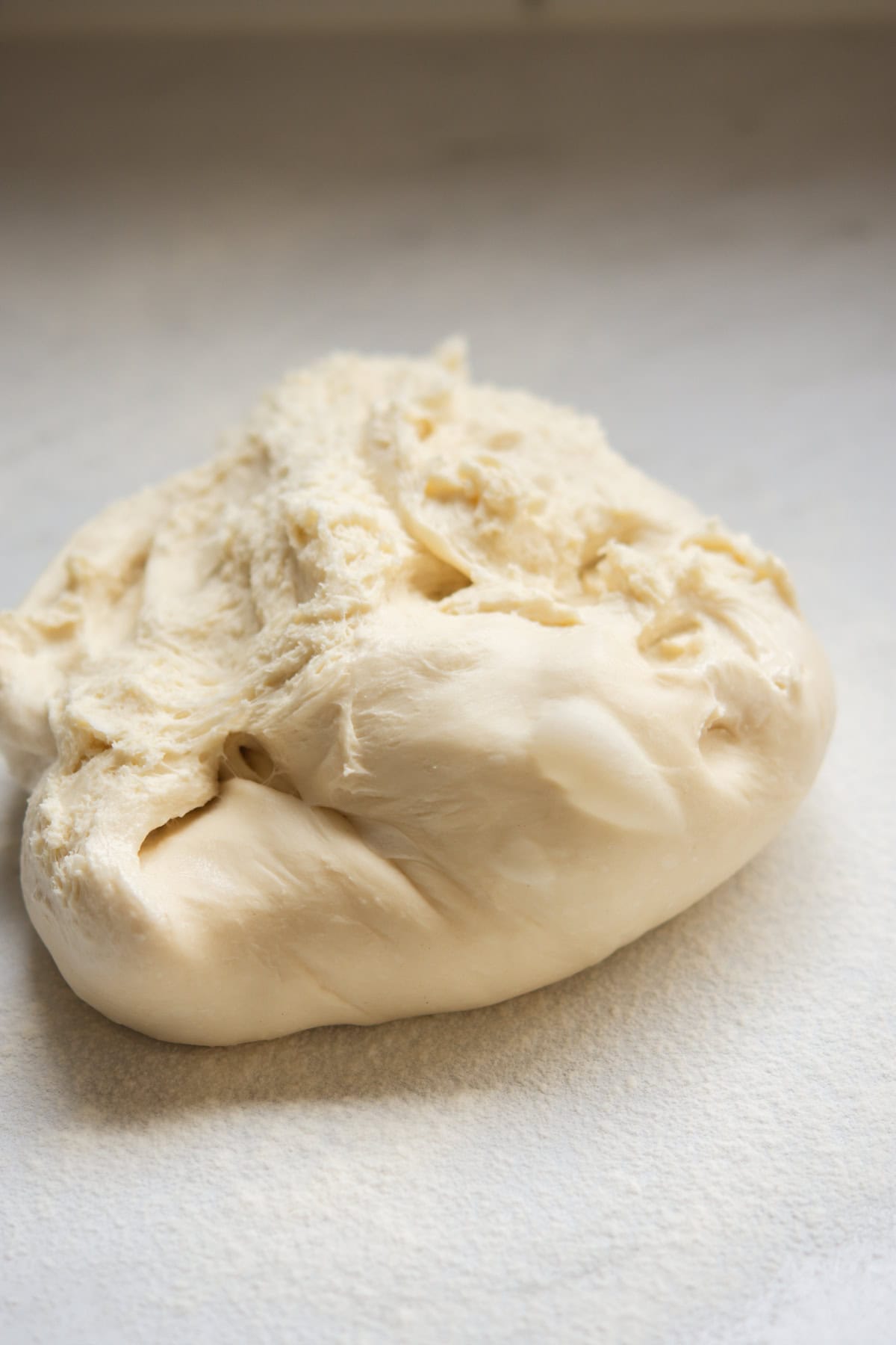 A close-up of a ball of raw bread dough resting on a lightly floured surface, with a soft and slightly sticky texture.