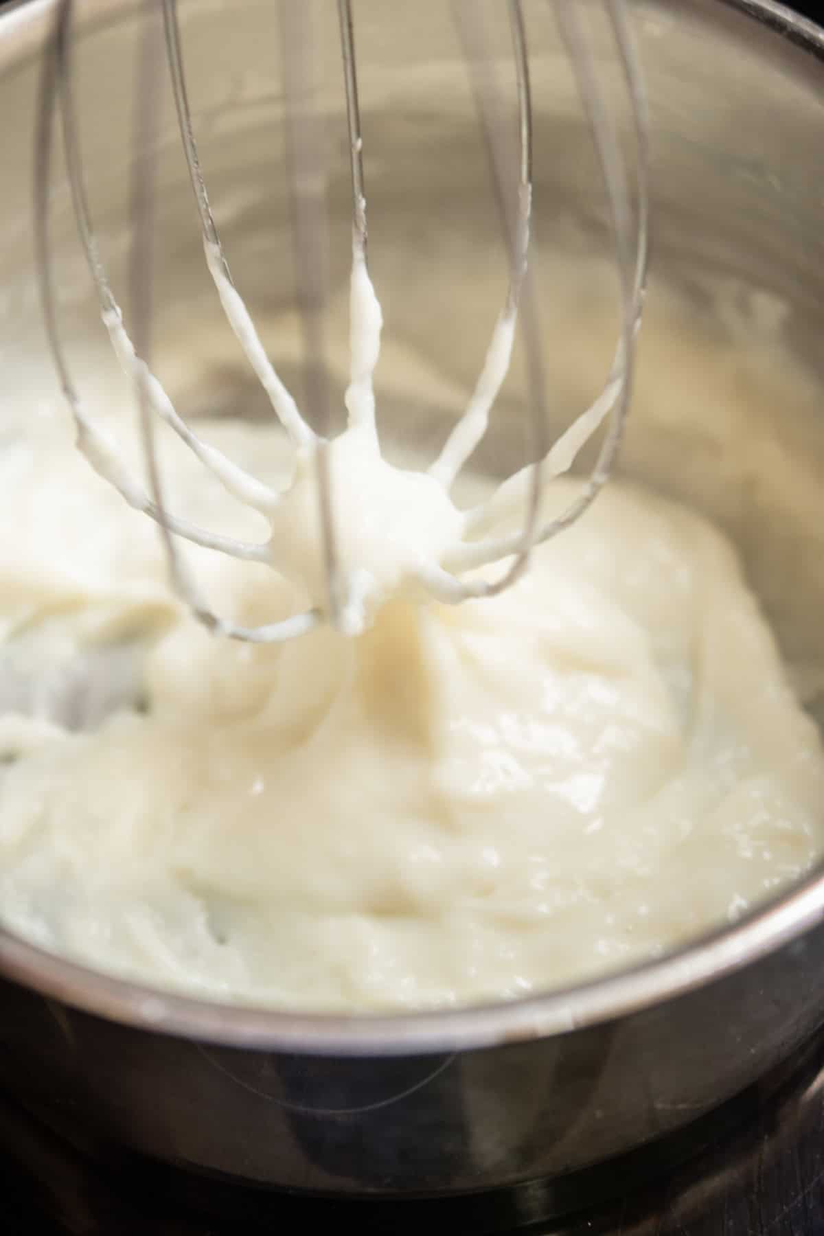 A metal whisk mixing thick tangzhong in a stainless steel bowl.