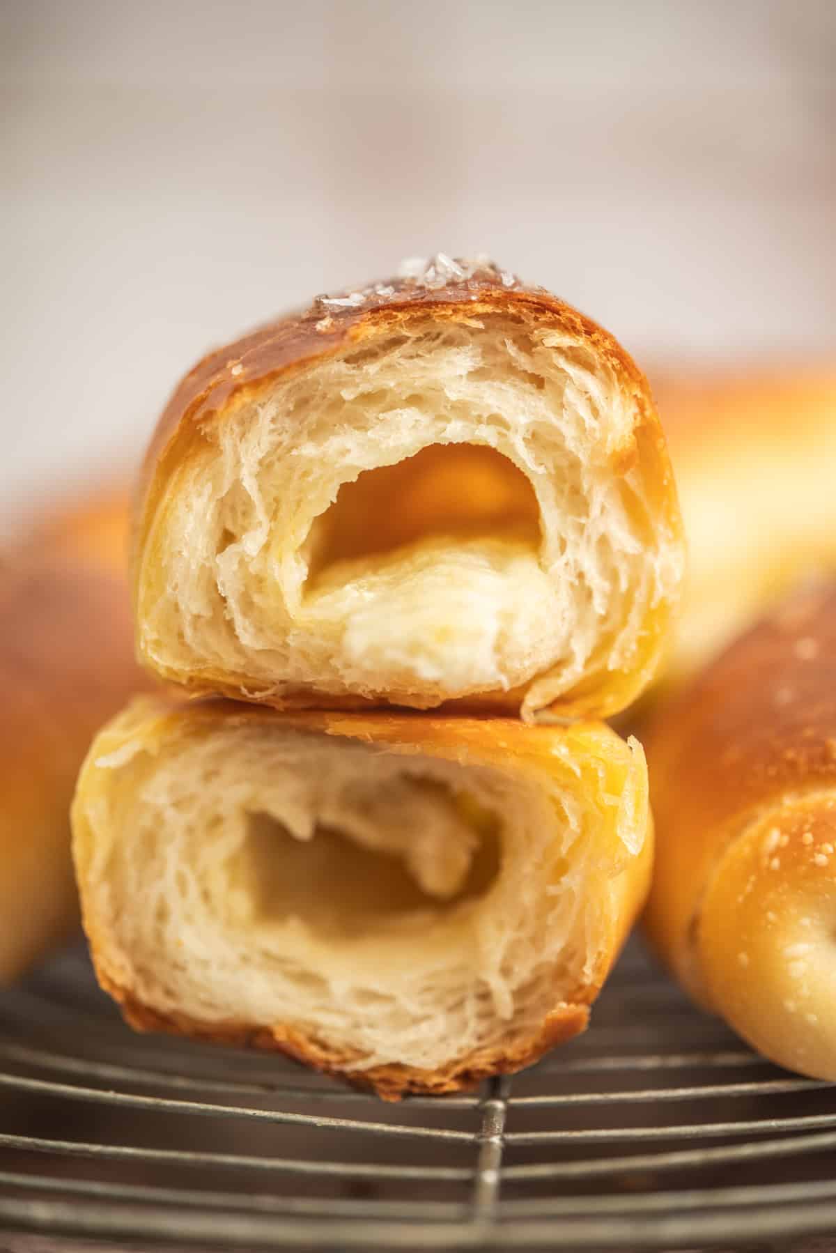 Close-up of two stacked, golden-brown Sourdough Salt Bread pastries with airy, hollow centers, placed on a wire rack. The texture appears crisp on the outside and soft on the inside.