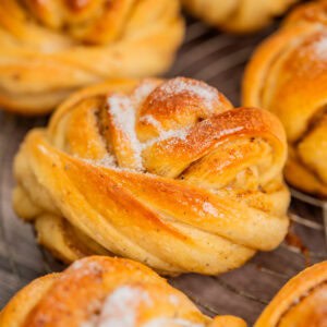 Close-up of golden brown, twisted cardamom buns topped with a sprinkle of sugar, arranged on a wire cooling rack.