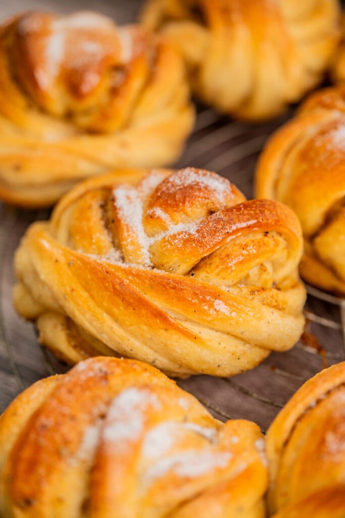 Close-up of golden brown, twisted cardamom buns topped with a sprinkle of sugar, arranged on a wire cooling rack.