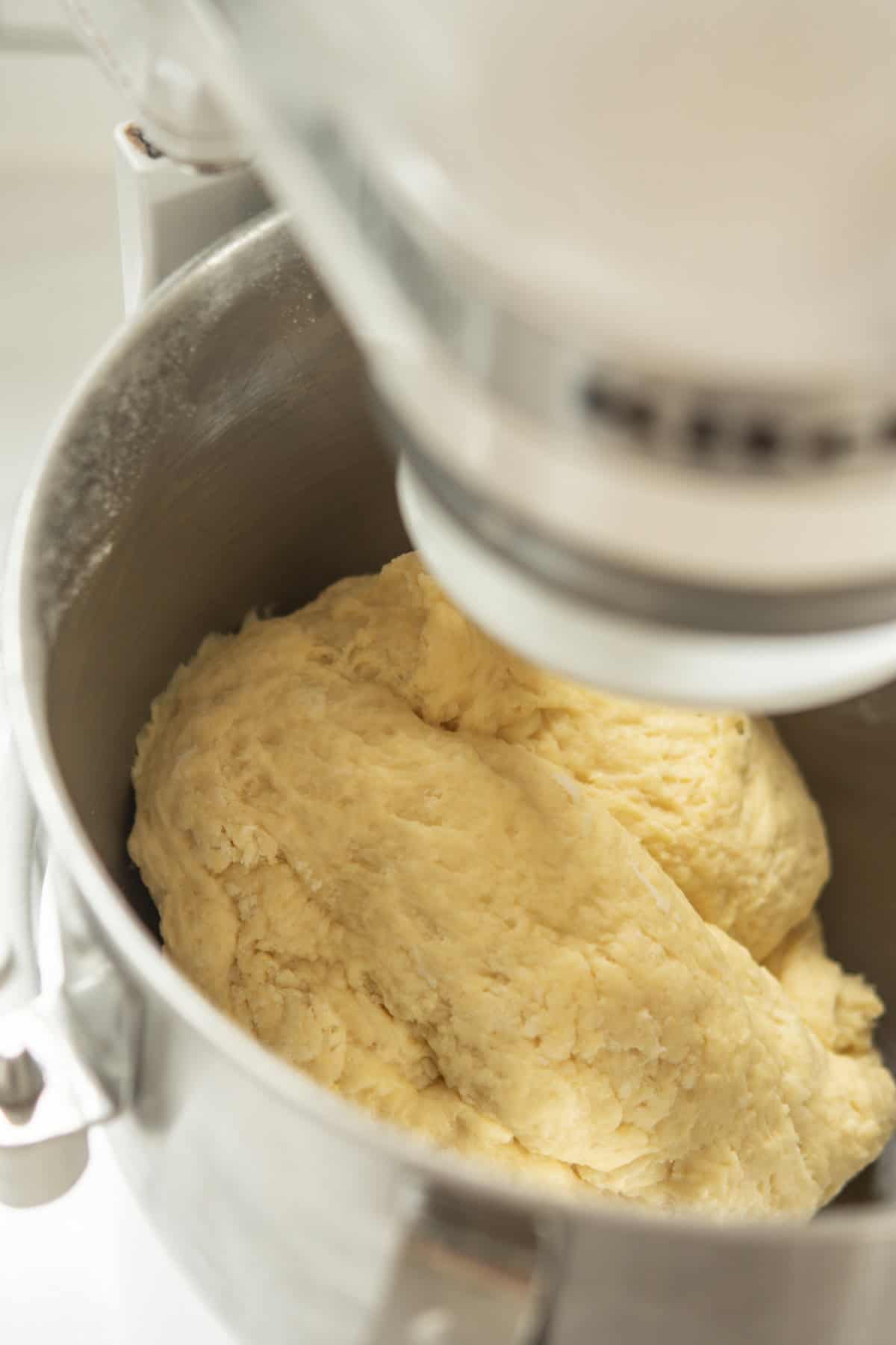 Close-up of bread dough mixing in a stand mixer bowl, showing the doughs rough texture as it is being kneaded by the machine.