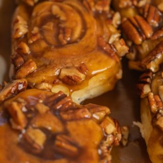 Close-up of sourdough sticky rolls covered in a glossy caramel sauce and topped with chopped pecans. The rolls look soft, gooey, and freshly baked.