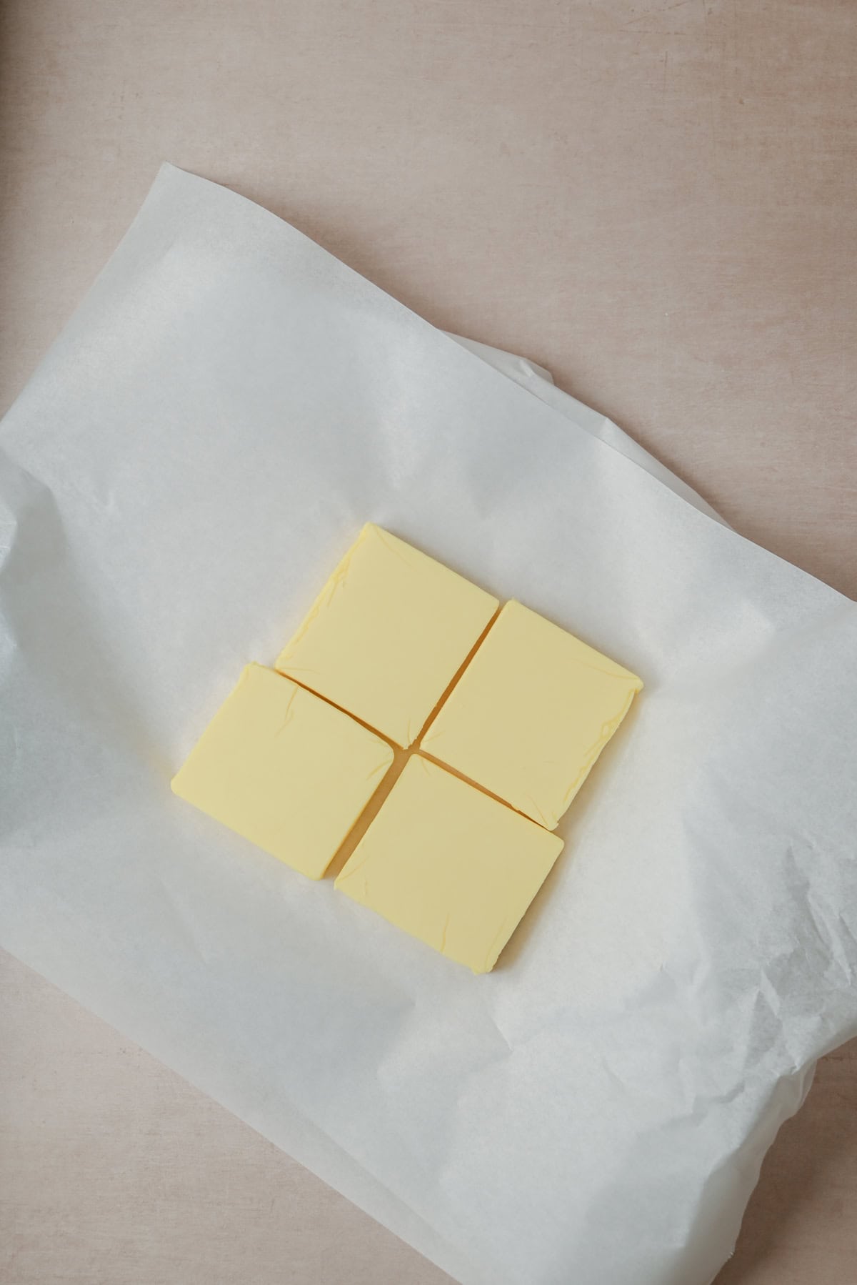 Four square pieces of butter arranged in a square shape, placed on a sheet of white parchment paper on a light-colored surface.