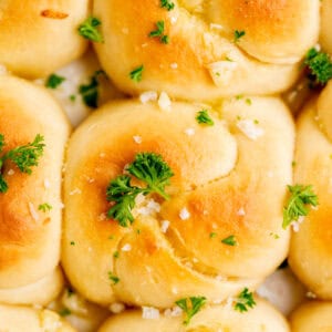 Golden brown sourdough garlic knots topped with chopped parsley and coarse salt, closely arranged together in a baking dish.